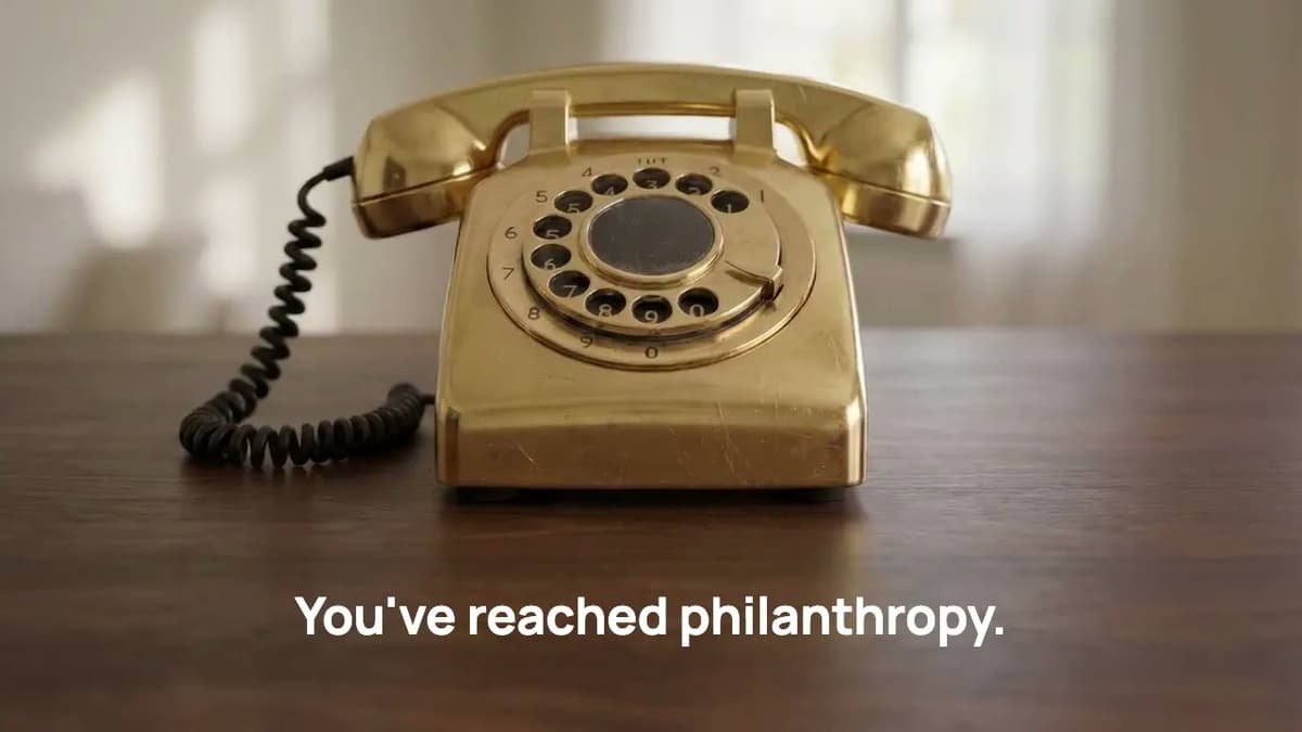 A gold rotary telephone on a wooden table, with the words You’ve reached philanthropy.